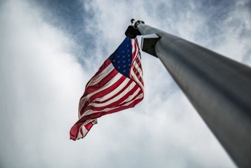 An American flag waving on a flagpole against a cloudy sky seen from below