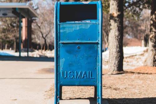 A blue USPS mail box with trees in the background